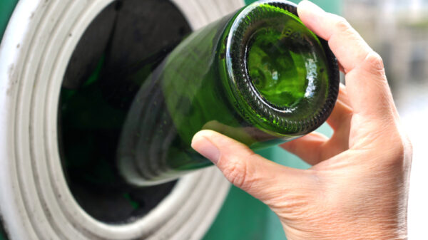 Image showing a person throwing a glass bottle into a recycling container - the UK government has disallowed glass from Scotland's deposit return scheme