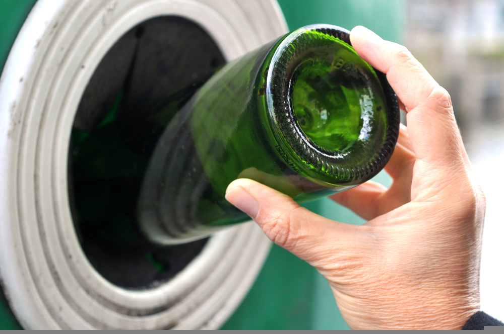 Image showing a person throwing a glass bottle into a recycling container - the UK government has disallowed glass from Scotland's deposit return scheme