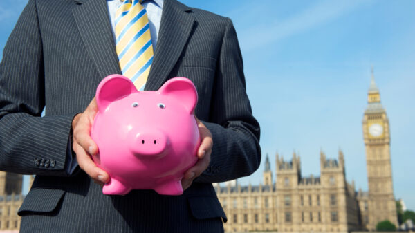 British politician holding a classic pink piggy bank in front of the government Houses of Parliament in London, UK