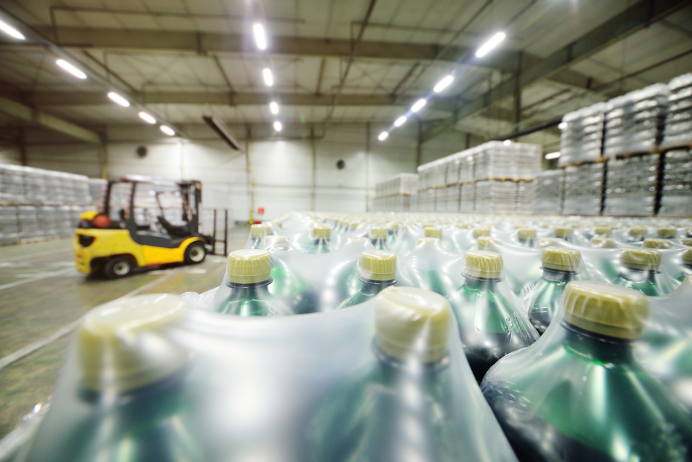 Yellow loader on the background of a huge industrial food warehouse with plastic PET bottles with beer, water, drinks. plastic packaging concept