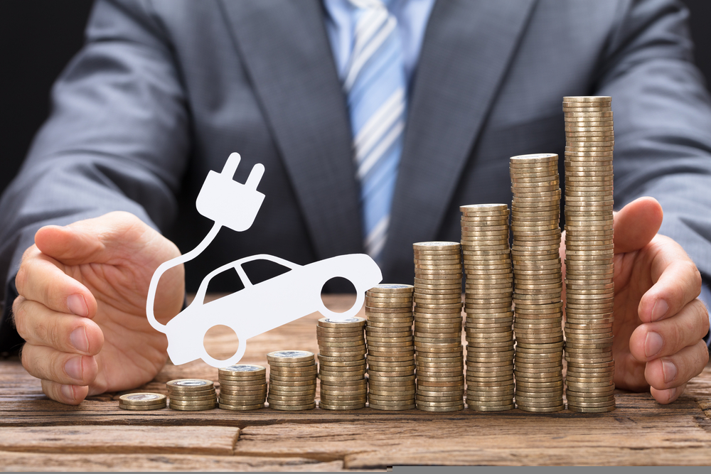 Midsection of businessman protecting coins with electric vehicle at wooden table