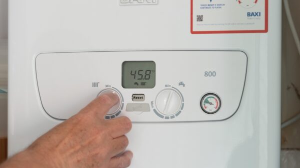 Man's hand turning down the dial on a gas boiler central heating system. Cost of utility bills soars.